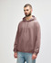 A person stands wearing a pink hooded sweatshirt with a front pocket and a drawstring hood.