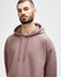 A woman wearing a pink Gildan Softstyle adult hooded sweatshirt, with her hands near the hood.