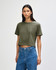 A woman wears an olive green boxy t-shirt, styled with light blue jeans, against a plain background.