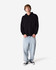 A unisex black hooded sweatshirt is worn with light blue baggy jeans and black sneakers, featuring a logo.