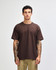 A model wears a brown American Apparel Super Heavyweight T-Shirt, featuring a relaxed fit and a logo.