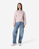 A light pink women's crewneck sweatshirt paired with blue wide-leg jeans and white sneakers. The sweatshirt has a logo.
