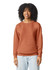 A woman wears an orange-brown lightweight crewneck sweatshirt, featuring a relaxed fit and long sleeves.