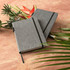 A grey A5 notebook with a textured cover, featuring a black elastic band, displayed alongside tropical foliage.