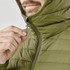 A close-up of a person pulling the zipper on a green thermal jacket, featuring a hood and quilted design.