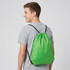 A green drawstring bag is worn on the back of a person, featuring black straps and a simple design.