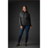 A woman wearing a black hybrid jacket with a padded front and textured sleeves, paired with denim jeans.