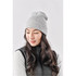A grey knit beanie worn by a woman with long, wavy hair, paired with a dark vest. It features a logo.