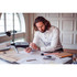 A man with long hair wearing a white button-up shirt, sitting at a desk with architectural plans and tools.