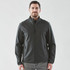 A man wearing a dark grey softshell jacket with a zip front and side pockets. The jacket has a logo.