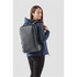 A woman wearing a navy jacket carries a grey Hedmark Commuter Backpack, featuring multiple compartments and a logo.