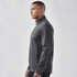 A man wearing a grey lightweight softshell jacket with a high collar and zippered pockets, featuring a logo.