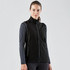 A black softshell vest with a zip front and side pockets, worn over a long-sleeve top. The model has a neutral expression.