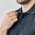 A close-up of a man's hand adjusting the collar of a black polo shirt featuring buttons and a logo.