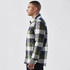 A men's quilted shacket in green, grey, and navy check pattern, featuring a side view of the model.