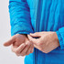 A blue quilted jacket with a close-up of a man's hand adjusting the cuff. The jacket features a logo.
