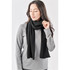 A woman models a black knit scarf, styled casually with a grey top. The scarf has a soft texture and falls loosely.