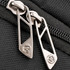 Close-up of silver zippers on a black backpack, featuring a branded logo on the zipper pulls.