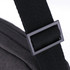 A black shoulder strap buckle featuring a textured fabric. The strap connects to a dark grey bag.