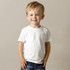 A smiling child in a white organic crew neck T-shirt, paired with denim jeans. The shirt has a logo.