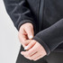 A close-up of hands adjusting the cuffs of a black polar fleece jacket, featuring a logo.