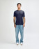 A model stands wearing a navy American Apparel Tri-Blend T-shirt and light blue jeans, with white shoes.