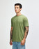 A unisex T-shirt in olive green, featuring a relaxed fit and short sleeves, displayed on a model with tattoos.
