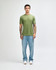 A unisex t-shirt in olive green, paired with light blue jeans, worn by a model with tattoos.