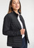 A women's tailor jacket in black, featuring a quilted design and a zip closure. A model is wearing it with a white shirt.