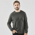 A man poses in a long-sleeve tee in dark green, paired with black pants, featuring a logo on the shirt.
