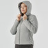 A woman is wearing a grey puffer jacket with a hood, featuring a zip-up front and a fitted silhouette.
