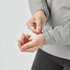 A woman's hand adjusts the cuff of a light grey thermal jacket. The jacket features a fitted design with a logo.