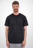 A man stands wearing a plain black short sleeve tee, with a neutral background. The tee features a logo.