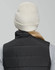 A cream beanie with a ribbed design, worn by a person in a black vest. The back of the beanie is visible.