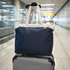 A navy blue tote bag with cream handles positioned on top of a suitcase in an airport setting.