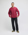 A red crew sweatshirt is worn by a model standing in a casual pose, paired with dark trousers and green shoes.