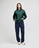 A green sweatshirt paired with navy trousers, featuring a logo on the sweatshirt. The model stands against a light background.