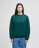A green crewneck sweatshirt with a logo, displayed on a model wearing blue jeans.