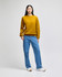 A model wearing a mustard yellow crewneck sweatshirt paired with light blue jeans and white shoes, featuring a logo.