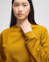 A model wears a mustard yellow Champion Powerblend® adult crewneck sweatshirt with a logo on the sleeve.