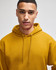A mustard yellow pullover hooded sweatshirt with a drawstring hood, worn by a model. It features a logo on the garment.