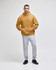 A hooded sweatshirt in a warm mustard colour paired with light grey sweatpants. The model is standing confidently.