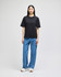 A black Champion Adult Heritage Jersey T-shirt displayed on a model wearing blue jeans and white sneakers.