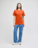 An orange short-sleeve t-shirt worn by a model, paired with blue jeans and white sneakers. The shirt features a logo.