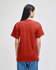 A red Champion adult short-sleeve t-shirt viewed from the back, worn with blue jeans. Features a logo.