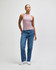 A woman in a lilac fitted tank top and blue jeans stands against a neutral background. The top features a logo.