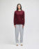 A long-sleeve t-shirt in maroon worn with grey sweatpants. The t-shirt features a logo on the sleeve.