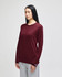 A maroon long-sleeve t-shirt worn by a model, paired with grey pants. The shirt features a logo.