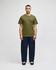 A model wearing an olive green short sleeve t-shirt and navy blue pants. The t-shirt features a logo.