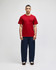 A red short sleeve t-shirt on a model, paired with navy pants, featuring a subtle logo on the sleeve.